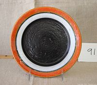 Front view of the ceramic plate showing the black center, white band, and orange rim with speckles.