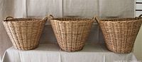 Front view of three wicker baskets side by side on a cloth-covered surface, showing their similar size and form.
