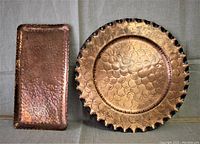 Two copper trays, one circular and one rectangular, placed side by side on a grey cloth background.