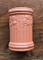 Side view of terracotta-colored cylindrical ceramic wine cooler with embossed grapevine decoration.