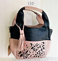 Front view of handbag showing black upper with pink floral cutout on front pocket and tassel decoration
