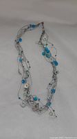 Full view of a multi-strand necklace laid out on a flat surface. The necklace has blue round beads, blue cube beads, small blue beads, and white irregular beads held by delicate silver-tone chains.