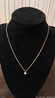 Full view of gold tone chain necklace with single cultured pearl pendant on a black velvet display stand.