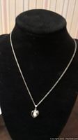 Front view of the cultured pearl necklace with silver tone chain and heart-shaped pendant showcased on a black display bust.