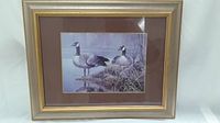 Framed print of two Canada geese near water with brown matting and silver-gold wooden frame.