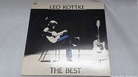 Front cover of Leo Kottke's 'The Best' vinyl LP album showing black and white photo of Leo Kottke with guitars.