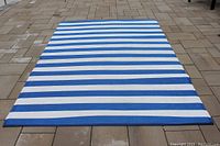 Photo showing full view of blue and white striped plastic patio rug laid out flat on a patio surface.