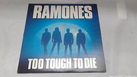 Front cover of Ramones Too Tough to Die LP showing band silhouettes and album title on blue background.