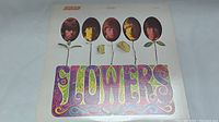 Front cover of The Rolling Stones Flowers vinyl LP showing the band members as flowers and colorful lettering.