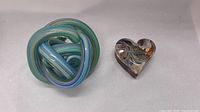 Photo showing the twisted ball-shaped glass sculpture and the heart-shaped glass sculpture placed side by side on a white background.