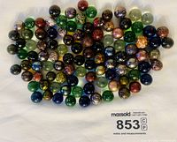 Top view showing approximately 100 assorted vintage glass marbles with dark colors and metallic flecked interiors, arranged in loose cluster on white background.