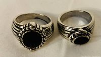 Two silver-tone men's rings with black centers displayed on white background.