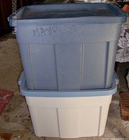 Two stacked Rubbermaid Roughneck storage bins, one gray with blue lid on top of a white bin with lid.