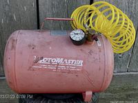 Front and side view of red Motomaster 5 gallon portable air tank showing logo and pressure gauge with yellow coiled air hose attached.