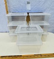 Stacked group of eight clear plastic storage tote containers with lids, showing front and side view with scale for size estimation.