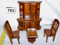 Front view of miniature wooden bookcase, table, and two chairs with measuring tape for scale
