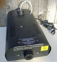 Photo of fog machine angled from top showing vents, warning label, power cord and fluid tube
