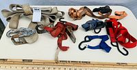 Photo of several heavy duty ratchet straps, tie-downs, and S-hooks laid out on a white table with a ruler for scale, showing different colors and sizes.