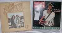Jimmy Buffett 'Recorded Live' and John Denver 'Back Home Again' vinyl album covers side by side on a surface.
