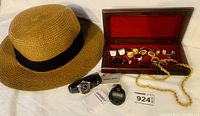 Photo showing straw hat, sport watch, electronic stopwatch, and wooden box open with cufflinks, rings, tie clips, and chain necklace inside