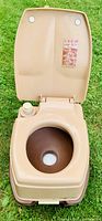 Beige portable camping toilet open view showing brown bowl and flush knob on left side of seat component.