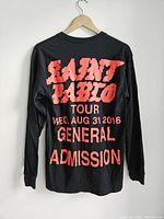 Back view of black long sleeve shirt with large distressed red text listing 'SAINT PABLO TOUR WED. AUG 31 2016 GENERAL ADMISSION'.