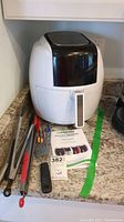 Electric air fryer with accessories including whisk, spatula, and tongs on countertop.