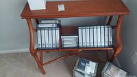 Photo showing wooden bookcase with curved sides and turned legs, with shelf holding VHS tapes (not included).
