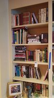 View of wooden bookshelf with five shelves filled with a large variety of books and some decorative items on bottom shelf.
