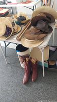 Overview of hats, boots, baseball bats, and waste can arranged on white tables and floor, showing all items in the lot