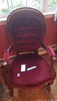Front view of the wood framed armchair with red velvet tufted upholstery, seat and arm cushions, and carved wood details.