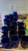 Various cobalt blue mugs and tumblers arranged on kitchen counter.