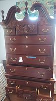 Front view of high boy dresser showing 11 drawers with brass drop handles and carved decorative panels