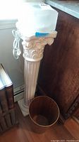 Full view of white ceramic pedestal with square light fixture on top and woodgrain can beside it.