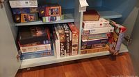 Photo showing a cabinet shelf with stacked puzzle boxes, including white boxes with black text, and colorful boxes with images promoting puzzle themes like wildlife and cats.