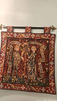 Full front view of medieval two figures tapestry mounted on rod with decorative loops.