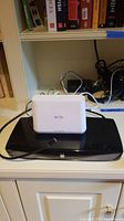 Photo shows a black TiVo DVR on a shelf with white Arlo controller sitting on top, cables visible behind.