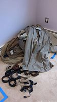 Pile of rain coats including trench coats in tan and neutral shades with assorted belts and suspenders spread on carpet.