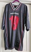 Front view of dark gray Buccaneers football jersey featuring large red number 19 with white and red trim around collar and sleeves.