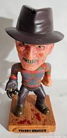 Front view of Freddy Krueger bobblehead showing detailed face, hat, clothing and the base with blood stains.