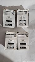 Four white boxes of Master Lock Commercial padlocks shown side by side, new condition packaging.