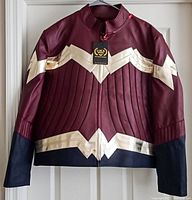 Front view of maroon leather jacket with gold Wonder Woman emblem detailing and black lower sleeves and bottom hem. Tag visible on collar.