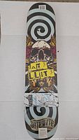 Photo of Satellite Reverb skateboard deck showing full graphic design with skull and spiral background, sealed in shrink wrap.