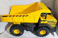 Side view of the Tonka Mighty Dump Truck showing solid yellow body, decals, large black rubber tires with yellow rims, and dump bed.