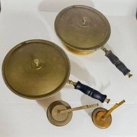 Top view of two brass chafing dishes with lids and black wooden handles, along with two small brass ladles in front.