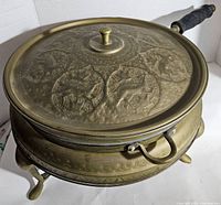 Angle showing embossed lid with animal designs and brass body of chafing dish.