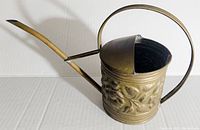 Side view showing the long curved spout, rounded handle, and embossed floral pattern on the brass watering can