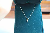 Front view of 16" chain and solitaire diamond pendant in open green velvet jewelry box.