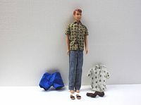 Full view of Ken doll with beige and green patterned shirt, blue shorts, cream-colored shirt, jeans, sandals, and brown shoes arranged around the doll.