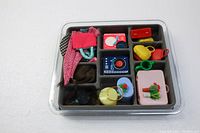 Top view of Barbie accessories contained in black tray including wigs, bags, toy record players, and hats.